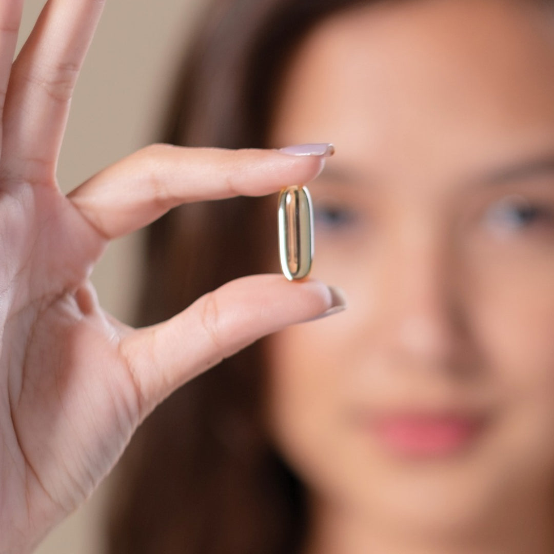 kvinne holder en omega-3 kapsel mellom fingrene